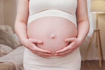 Fototapeta na wymiar Hands on the tummy of a pregnant woman, home living room
