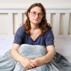 Portrait of an adult woman sitting on a bed with a blanket in a white bedroom. A brunette woman...