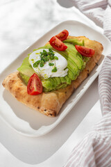 Avocado Sandwich with Poached Egg - sliced avocado and egg on toasted bread for healthy breakfast or snack, copy space.