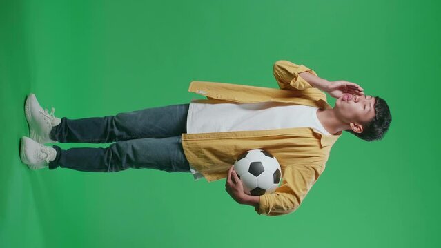 Full Body Side View Of Asian Boy With A Ball Making Fun Of The Losers By Ooh Face While Cheering Soccer On Green Screen Background
