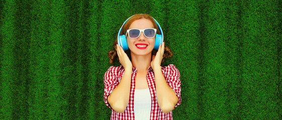 Portrait of happy smiling young woman listening to music in headphones relaxing lying on the grass...