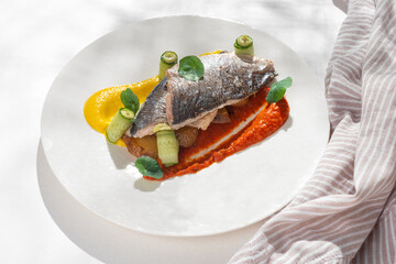 Fish dish - Dorado with rainbow creams. dorado fillet with garnish, greens and lemon on ceramic plate on white background for restaurant menu.
