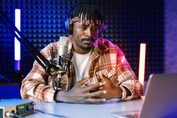 African radio host sitting at desk recording in studio with microphone and laptop