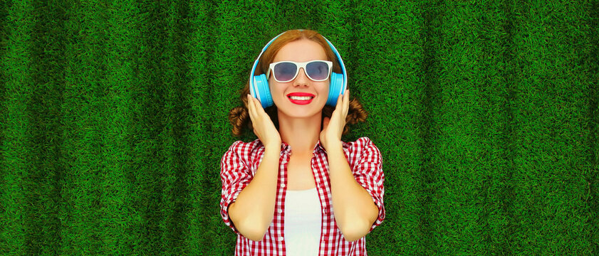 Portrait Of Happy Smiling Young Woman Listening To Music In Headphones Relaxing Lying On The Grass Background In Summer Park