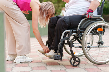 Young unrecognizable female helping woman patient with disability sitting on wheelchair