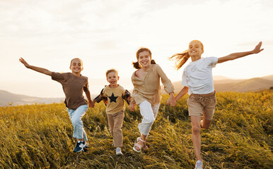 Group of happy joyful school kids boys and girls running with holding hands  in field on sunny day