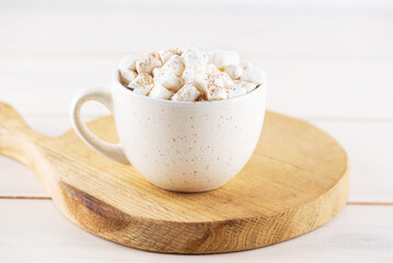 Coffee with marshmallows and cinnamon in a mug on a wooden board.