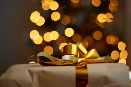 Image of Christmas gift box with gold bow on background of defocused golden lights on New Year tree. Congratulating friends and family with New Year holidays. Merry Christmas.