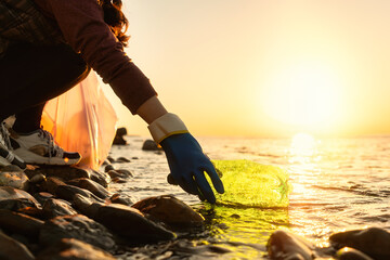 Coastal cleanup and garbage collection for recycling. A woman volunteer collects plastic bottle by the sea or river, closeup of hand. Low angle view. World environment day and Earth day concept