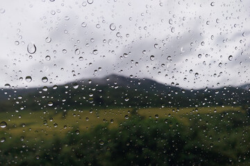 Raindrops on the glass with the blurred landscape background.
