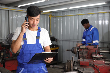 Multiethnic technician mechanic using metal lathe machine operate polishing car disc brake with smart mobile phone and clipboard at garage. Maintenance automotive and inspecting vehicle part concept