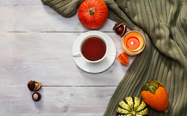 Autumn still life. Cup of tea, sweater, pumpkins, chestnuts and candle on wooden table. Details of still life in home interior. Concept: autumn season, fall background. Flat lay. Top view. Copy space.