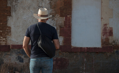Rear view of adult man holding bag against abandoned building