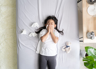 Top view Asian child girl sick with sneezing on the nose and cold cough on tissue paper because weak, Sick child with fever and illness in bed.