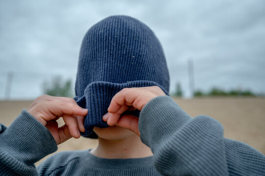 Playful Boy Covering Face With Knit Hat