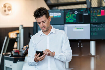 Businessman using smart phone in front of computer monitors