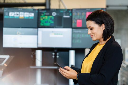 Smiling businesswoman using smart phone in front of computer monitors