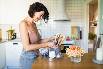 Smiling woman organizing spoons in container at kitchen counter