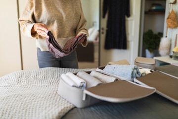 Hands of woman folding cloth on bed in bedroom