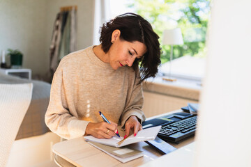 Mature businesswoman writing in note pad on table at home