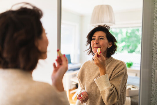 Mature Woman Looking In Mirror And Applying Lipstick