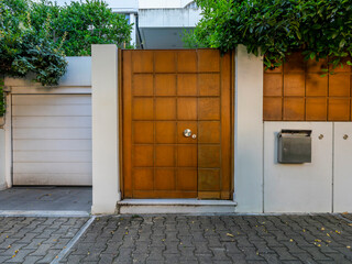 A modern house entrance, with a brown wooden door and fence wall by the sidewalk. Athens, Greece.