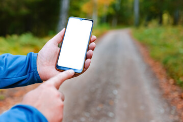Blank space mockup.Hiker man standing on a trail autumn forest and showing of smartphone white screen.Technology in nature concept.Selective focus.