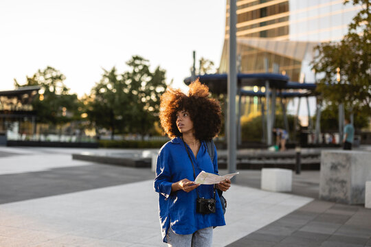 Woman with Afro hairstyle holding map on footpath