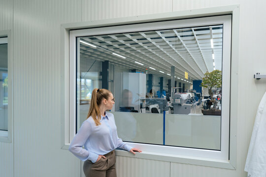 Young businesswoman with hand in pocket looking through window at warehouse
