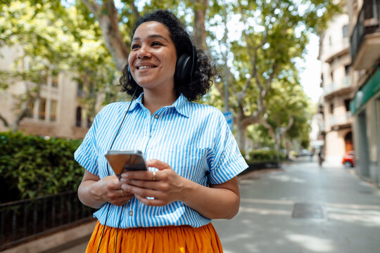 Smiling woman enjoying music through headphones on footpath