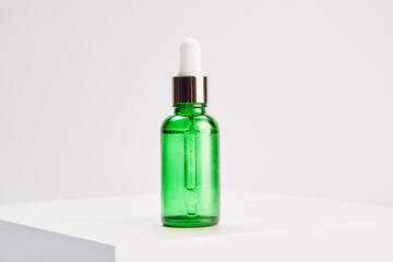 Green glass vial with gold dropper cap is on platform.