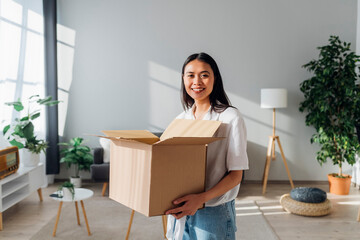 Smiling woman holding cardboard box standing in living room at new home