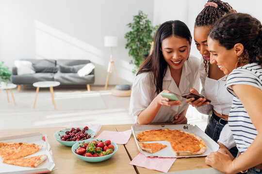 Smiling Friends Using Smart Phones In Kitchen