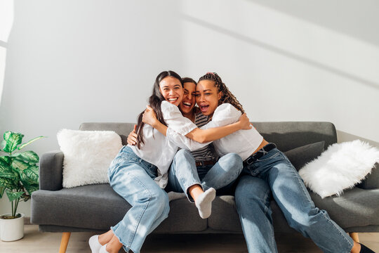 Happy Friends Embracing Each Other Sitting On Couch In Living Room