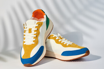 Stylish colorful shoes on white background with plant shadows, Trendy sneakers, Stylish fashionable...