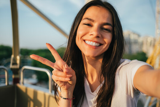 Happy woman showing peace gesture and taking selfie in Ferris wheel