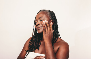 Elegant mature woman applying moisturizing cream on her face