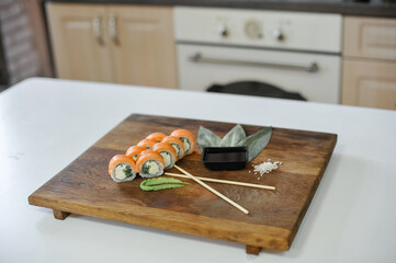 sushi rolls with salmon on kitchen table with chopsticks and red tablecloth.