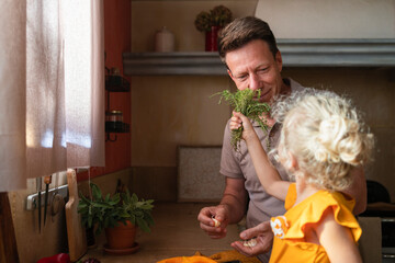 Girl holding thyme in front of father to smell in kitchen