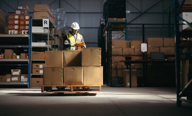 Logistics worker reading a clipboard while moving goods with a pallet jack in a warehouse