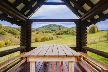 A place of rest for tourists in a mountain valley in autumn. Wooden gazebo, house on a background of green, yellow meadow and mountain peaks on a sunny day. 