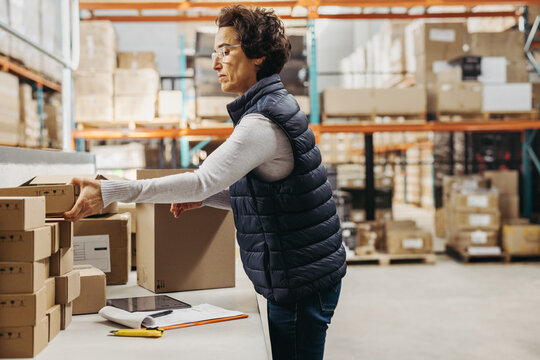 Female warehouse worker packing cardboard boxes while fulfilling online orders