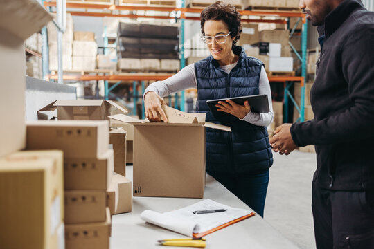 Manager and trainee packing cardboard boxes while fulfilling online orders