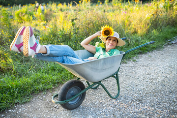 Happy mature gardener with sunflower lying in wheelbarrow