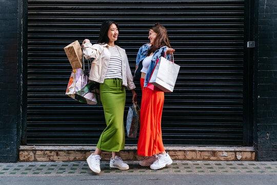 Happy lesbian women with shopping bags standing in front of shutter