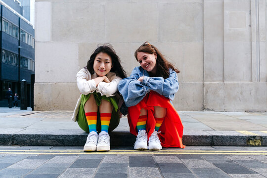 Smiling lesbian friends with multi colored socks sitting on footpath