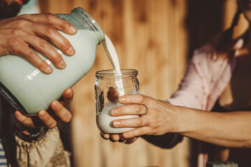 Man pouring fresh milk into glass jar on sunny day