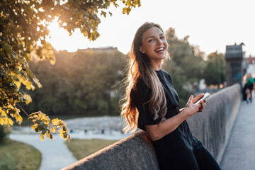 Cheerful woman with smart phone leaning on wall