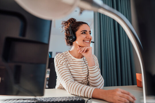 Smiling businesswoman with hand on chin wearing headset at desk in office