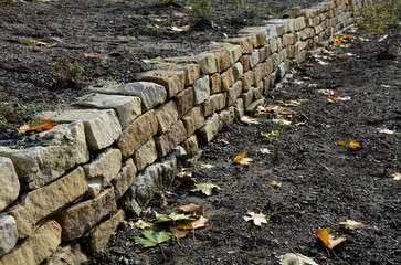 Fototapeta na wymiar the dry wall serves as a terrace terrace for the garden, where it holds a mass of soil. the wall is slightly curved, which helps it to stabilize better. planting perennials and rock gardens, gravel